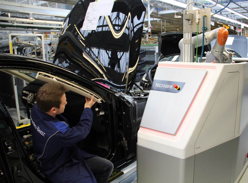 Mitarbeiter arbeitet gemeinsam mit einem kollaborativen Roboter und einer industriellen Maschinenverkleidung in der Fahrzeugmontage bei Mercedes-Benz.