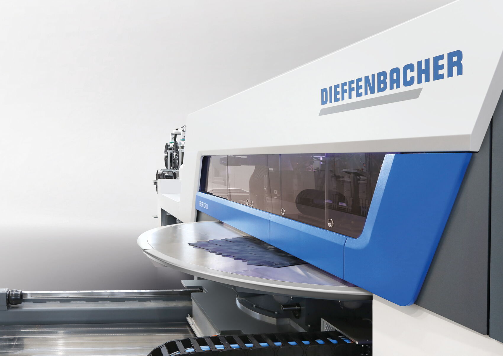 Nahaufnahme der Dieffenbacher Fiberforge Tapelegeanlage mit transparentem Prozessfenster und Drehtisch zur automatisierten Herstellung von Faserverbund-Layups im modernen Industrial Design.
